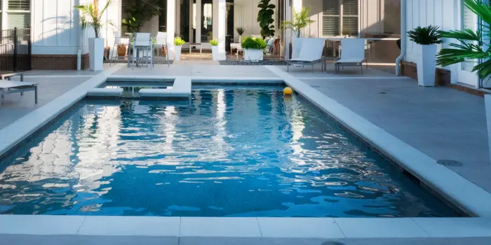 Close-up view of dark blue fibreglass pool water showing the shimmer on the curved steps and light beige travertine coping.