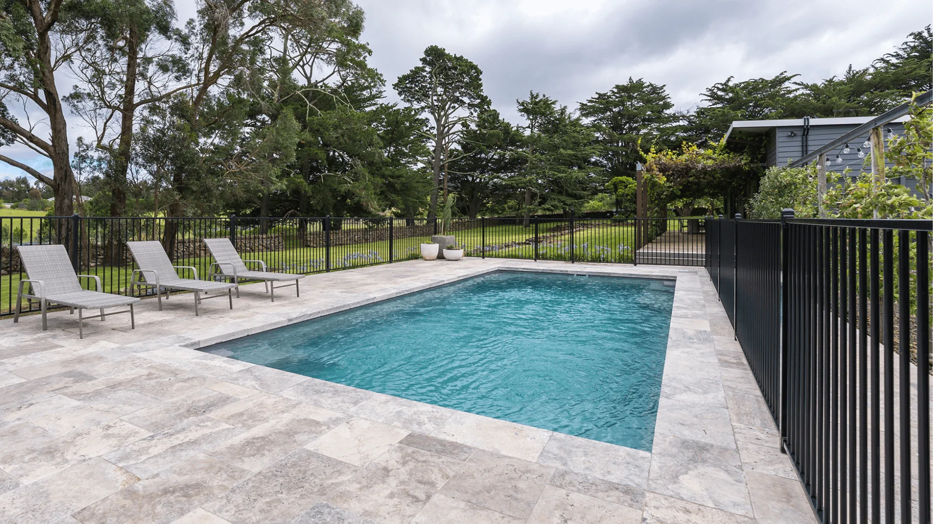Rectangular fibreglass swimming pool surrounded by stone tiles and lounge chairs, set within a landscaped area.